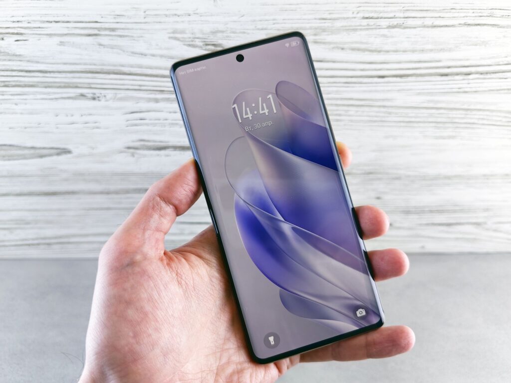 現在の画像: A detailed close-up of a hand holding a smartphone indoors, showcasing the screen in precise detail.