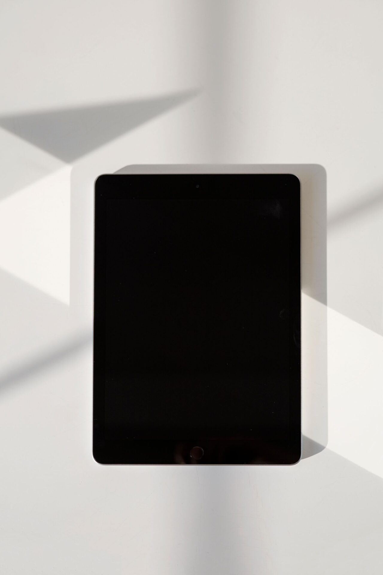 A digital tablet with a blank screen lies on a white surface in natural light.