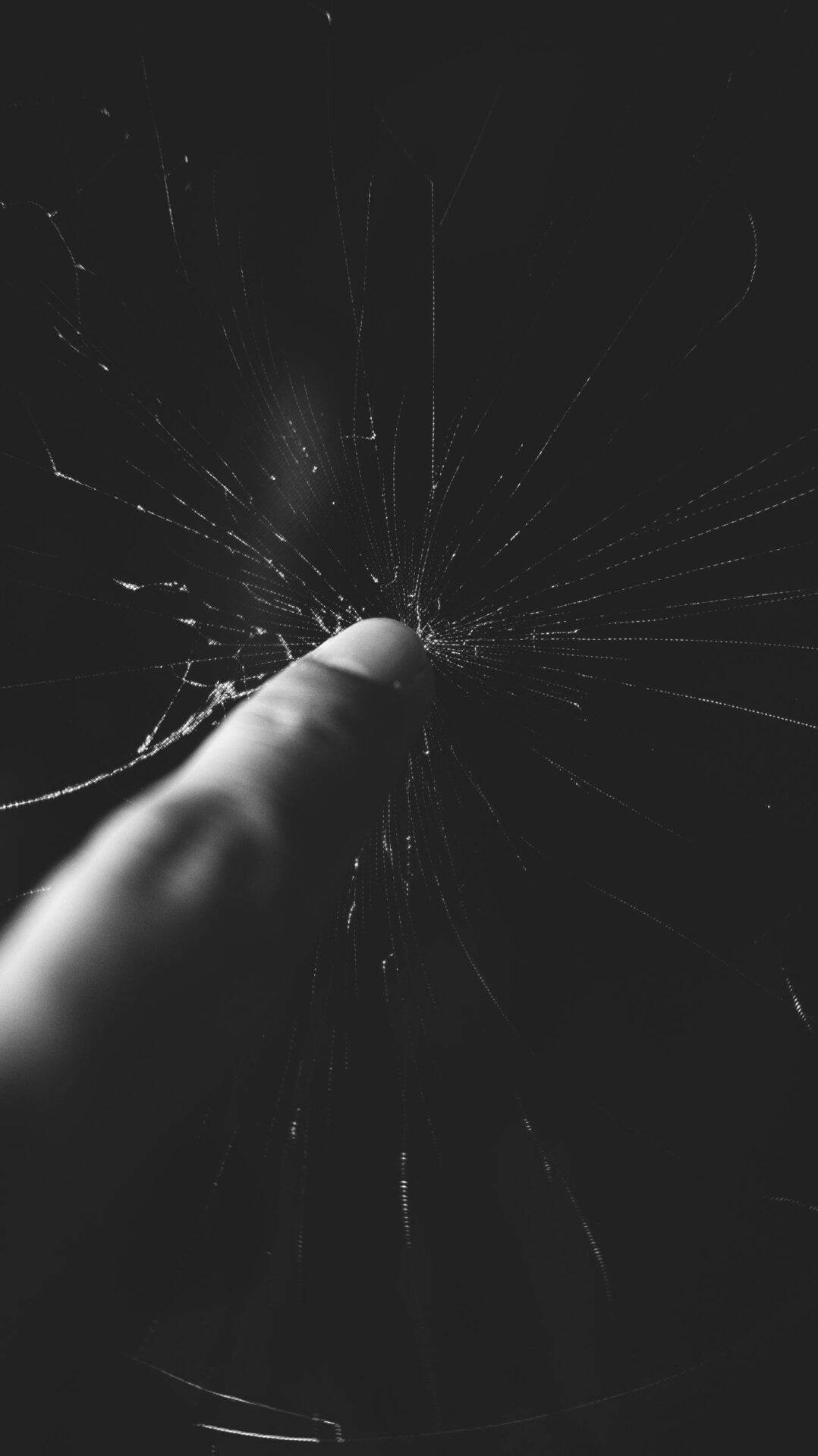 A dramatic black and white close-up of a finger touching cracked glass, emphasizing detail and texture.