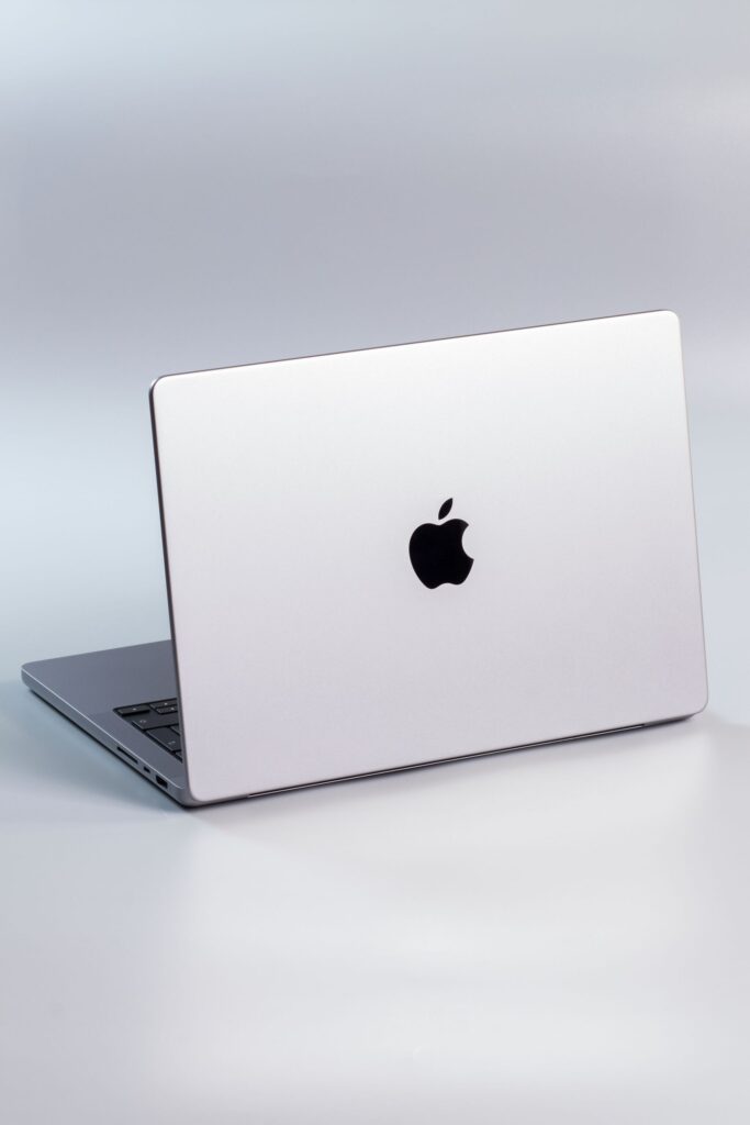 現在の画像: A modern silver laptop with a prominent logo on a minimalist studio background.