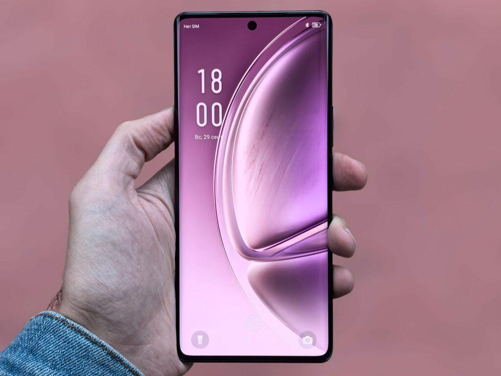 現在の画像: A person holding a sleek, modern smartphone with a purple screen against a plain background.