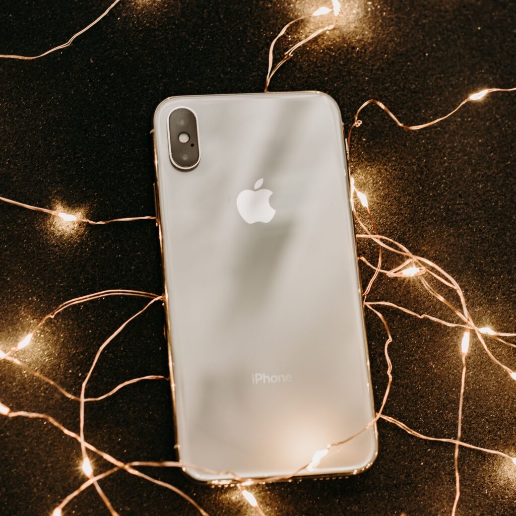 現在の画像: A sleek smartphone surrounded by glowing fairy lights on a dark surface for a luxurious effect.