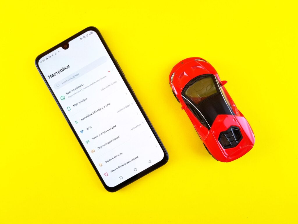 現在の画像: A smartphone and toy car placed on a bright yellow background viewed from above.