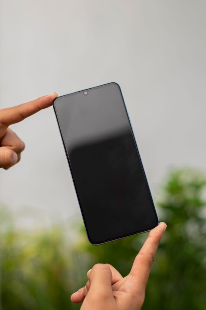 現在の画像: A smartphone balanced between two hands outdoors, showcasing modern technology.