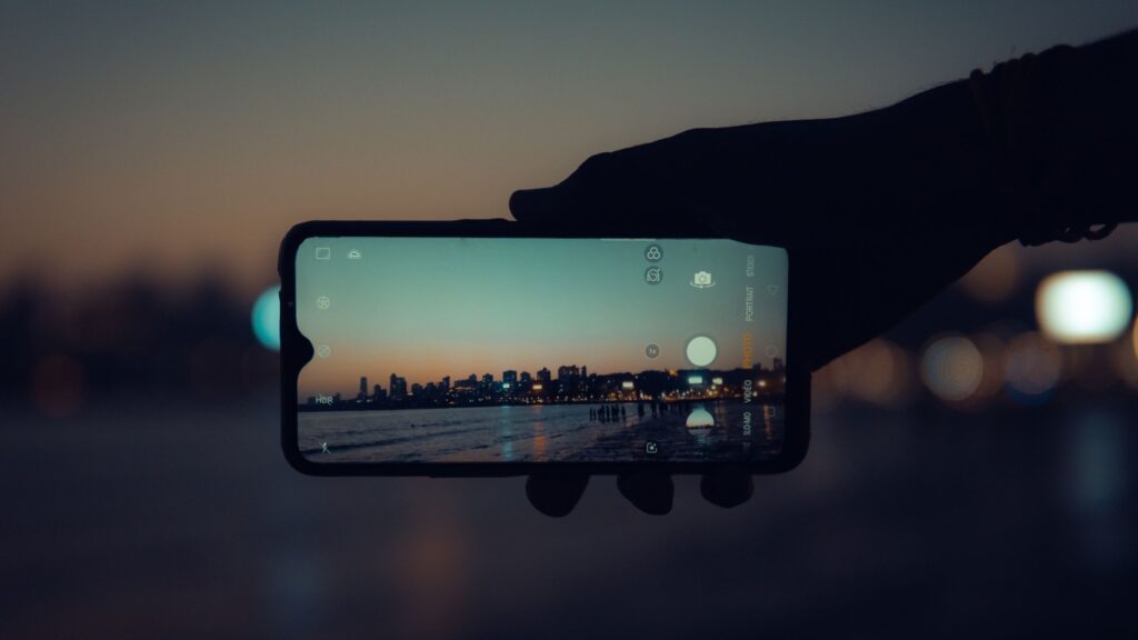 現在の画像: A smartphone capturing the Mumbai skyline at sunset with a clear reflection on its screen.