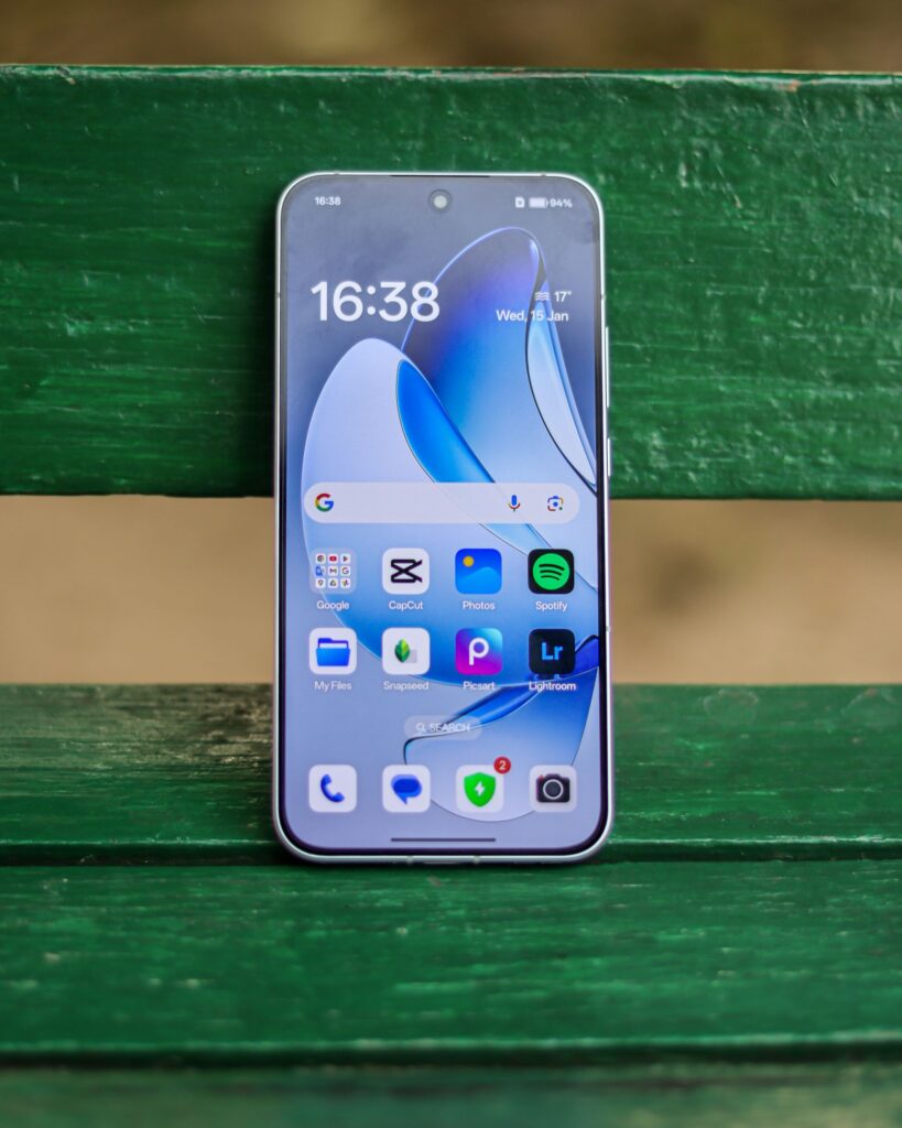 現在の画像: A smartphone showing various apps is placed on a green bench outdoors.