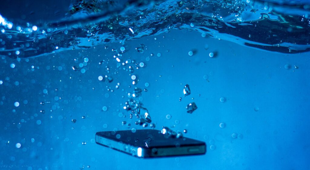 現在の画像: A smartphone submerged in water with bubbles rising around it, showcasing a dynamic underwater scene.