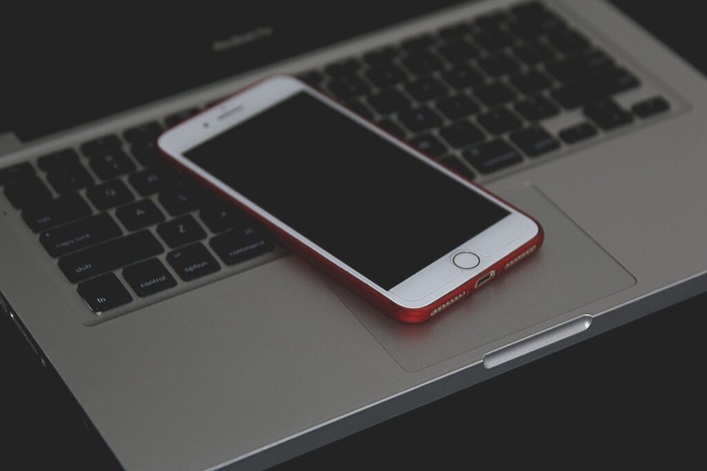 現在の画像: A smartphone with a red case resting on a laptop keyboard, showcasing modern technology indoors.