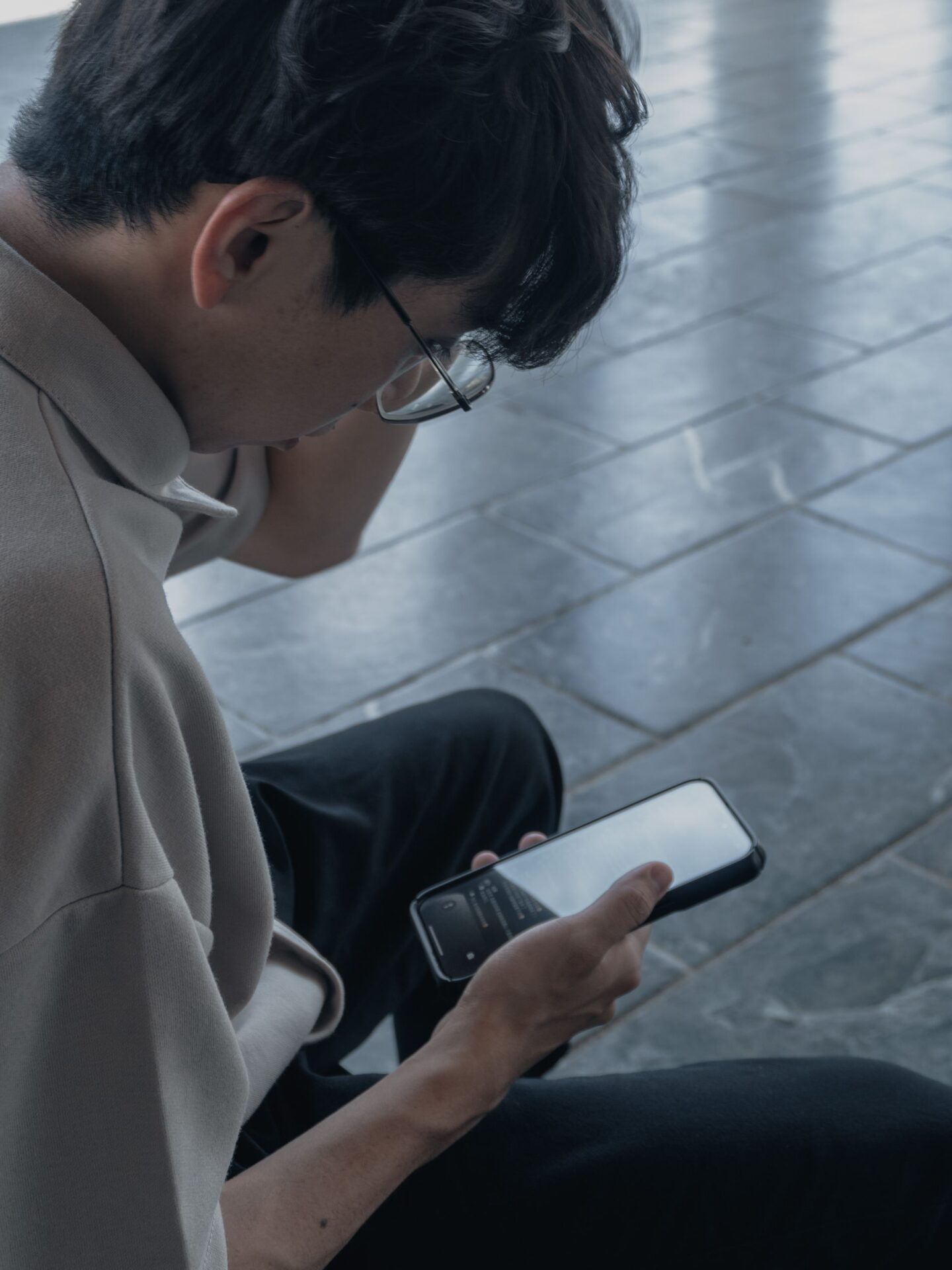 Asian man with glasses using a smartphone, captured in an urban environment.