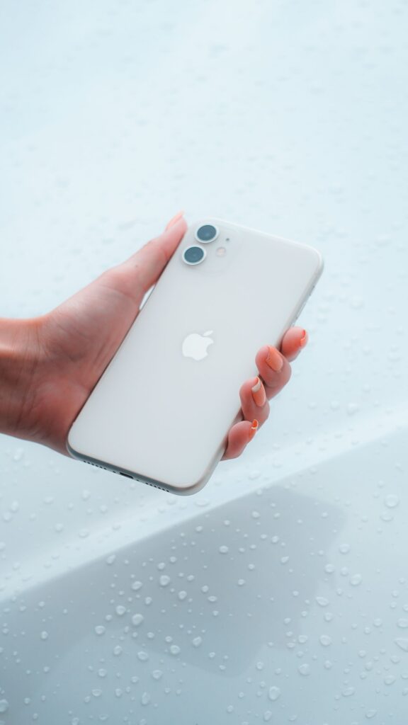 現在の画像: Close-up of a hand holding a white smartphone against a water droplet background.