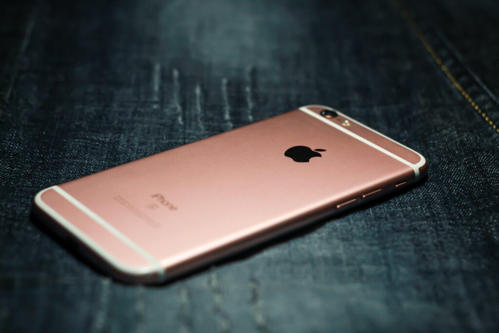 現在の画像: Close-up of a rose gold smartphone placed on dark denim fabric, highlighting tech style.