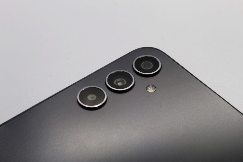 現在の画像: Close-up of a sleek smartphone with triple camera lenses and matte finish.