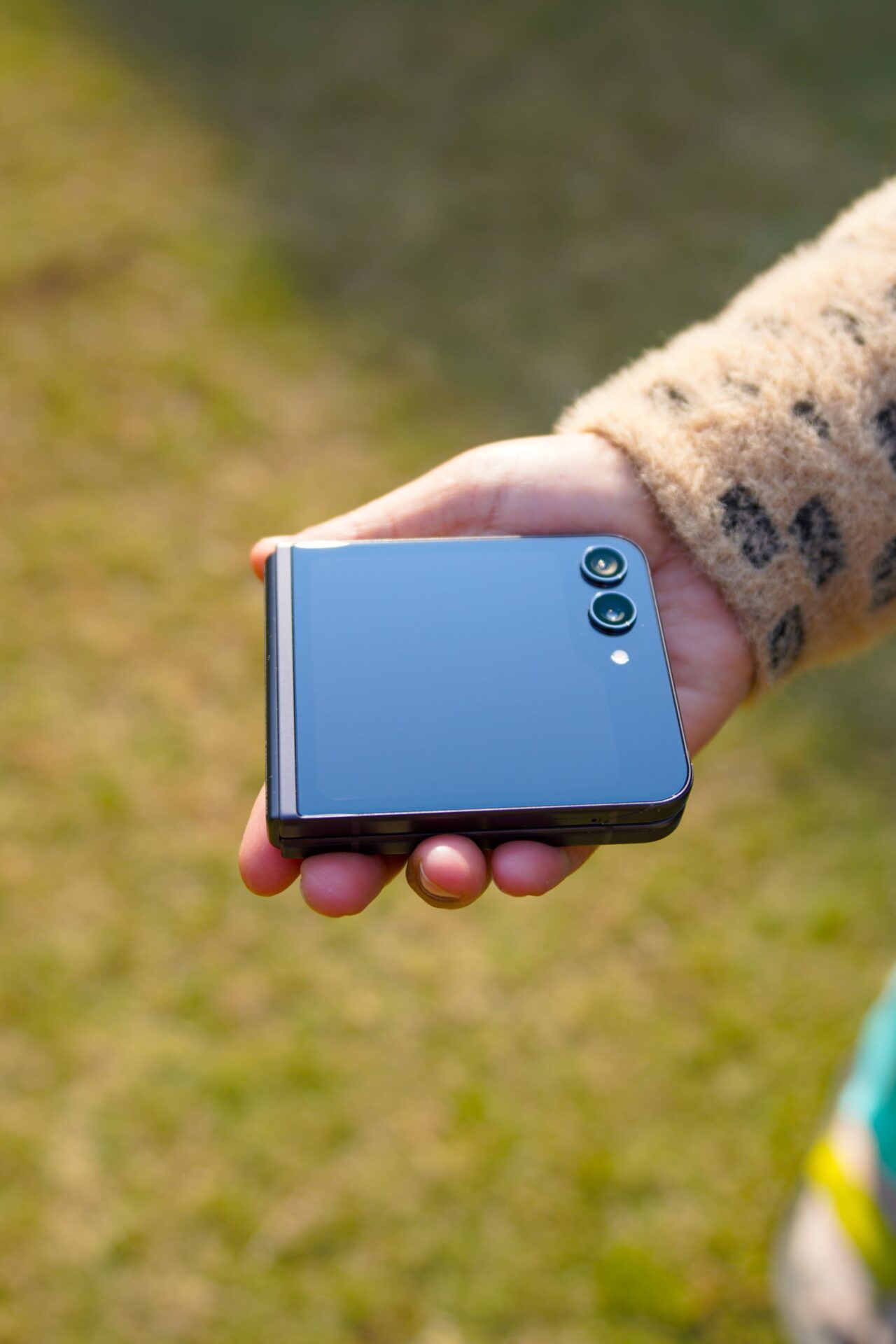 Close-up of a woman holding a foldable smartphone outdoors on a sunny day.