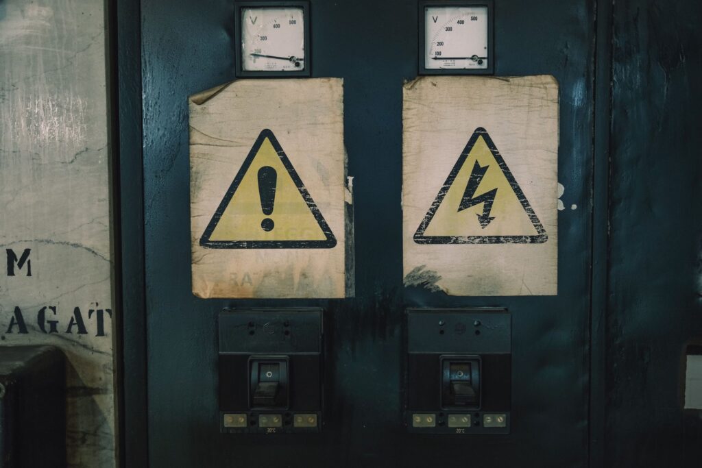 現在の画像: Close-up of industrial warning signs on an aged electrical panel.