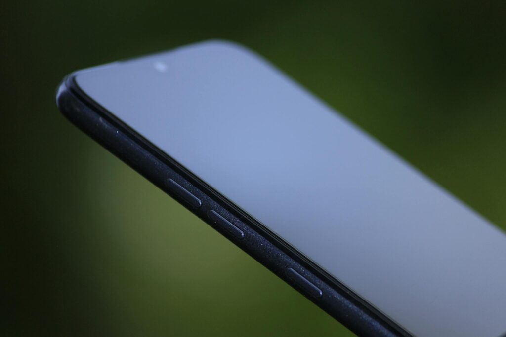 現在の画像: Close-up shot of a sleek black smartphone against a blurred green background, showcasing modern design.