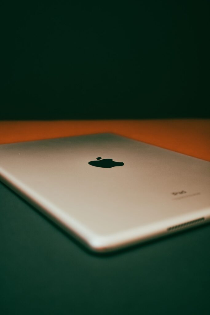 現在の画像: Close-up view of a silver tablet with iconic logo on a dark flat surface, showcasing modern technology.