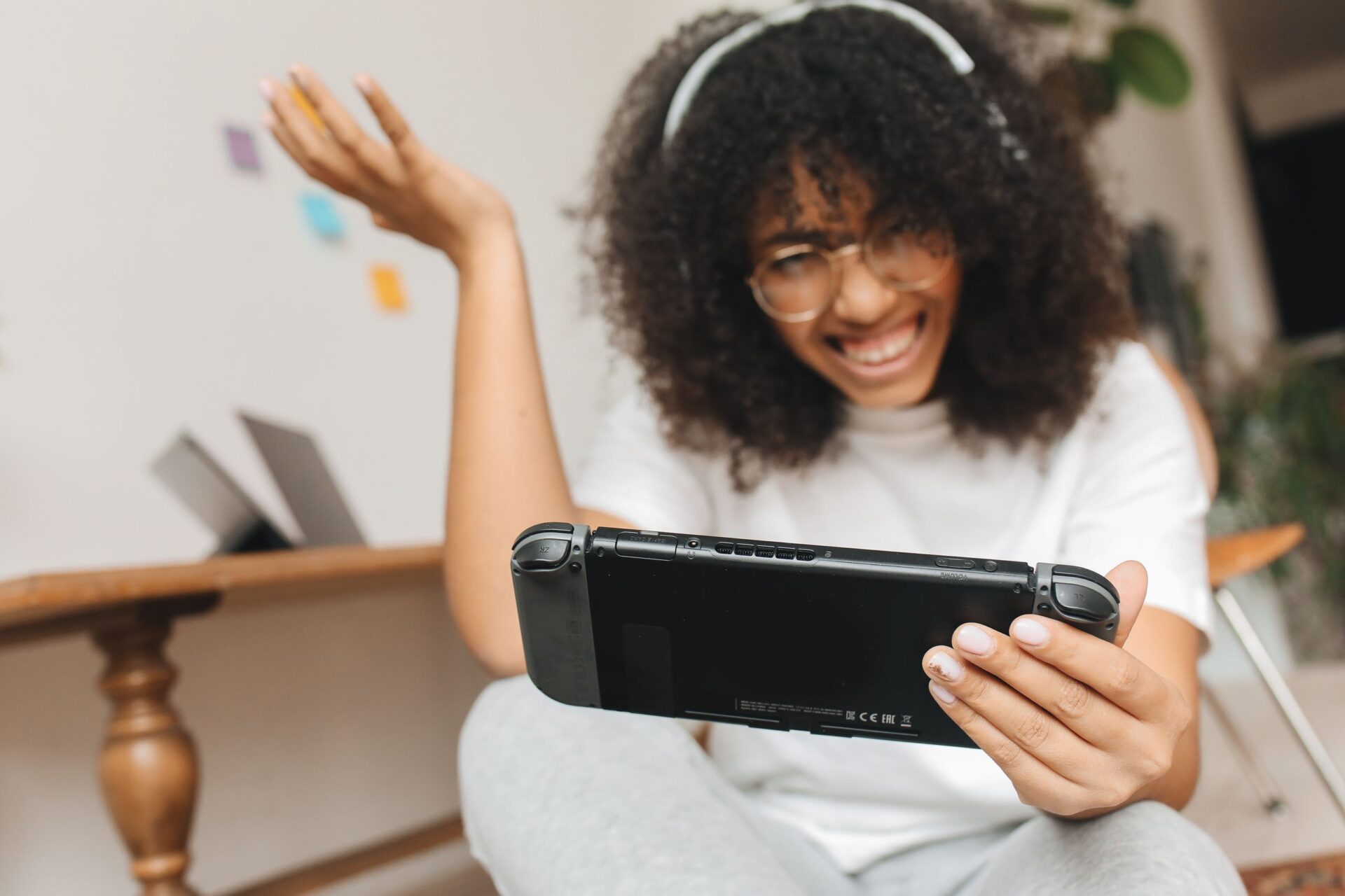 Curly-haired woman smiling while gaming indoors with a console, enjoying leisure time.