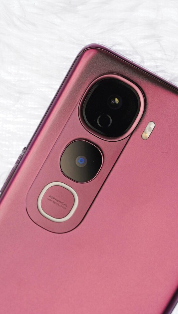 現在の画像: Detailed shot of a pink smartphone's back camera system, showcasing lenses and design.