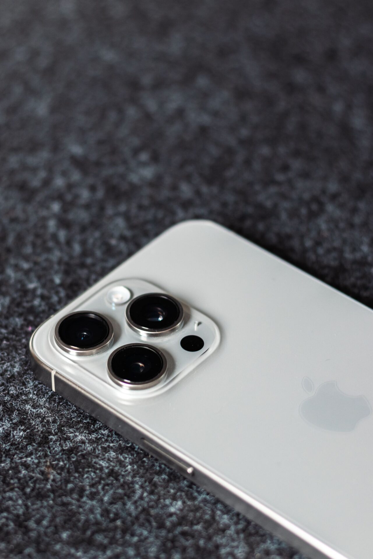 Detailed shot of a smartphone with triple camera lenses on a dark textured surface.