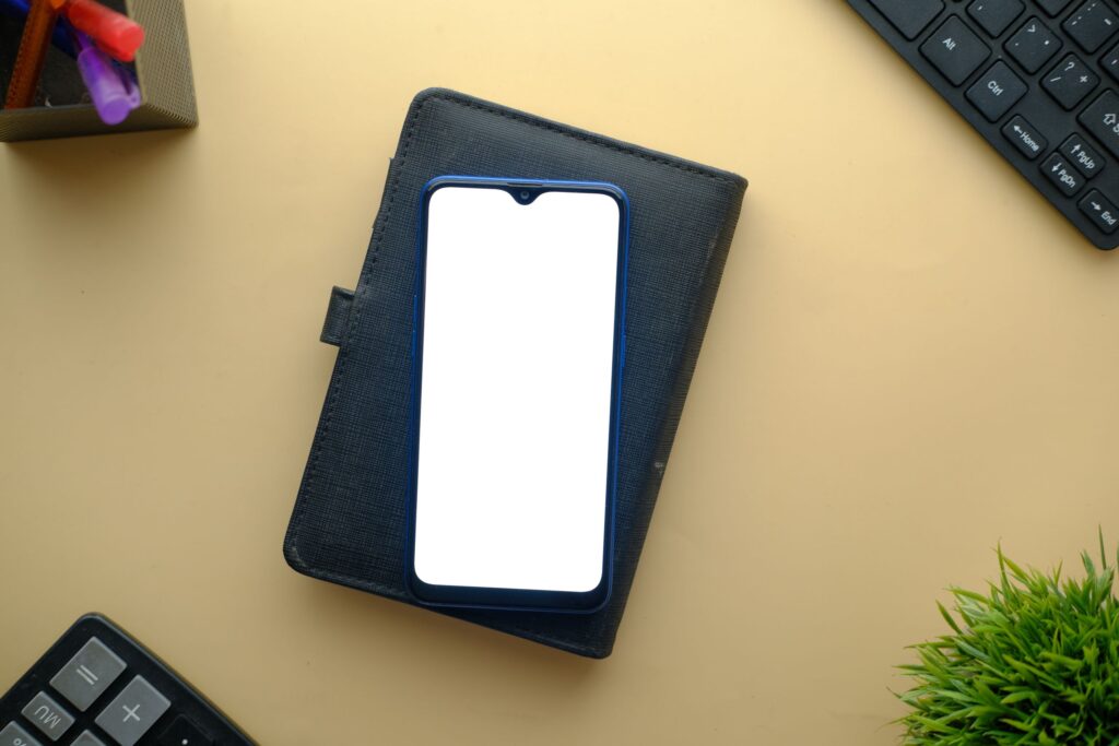現在の画像: Flat lay of smartphone with blank screen on styled desk with keyboard and plant. Perfect for mockup displays.