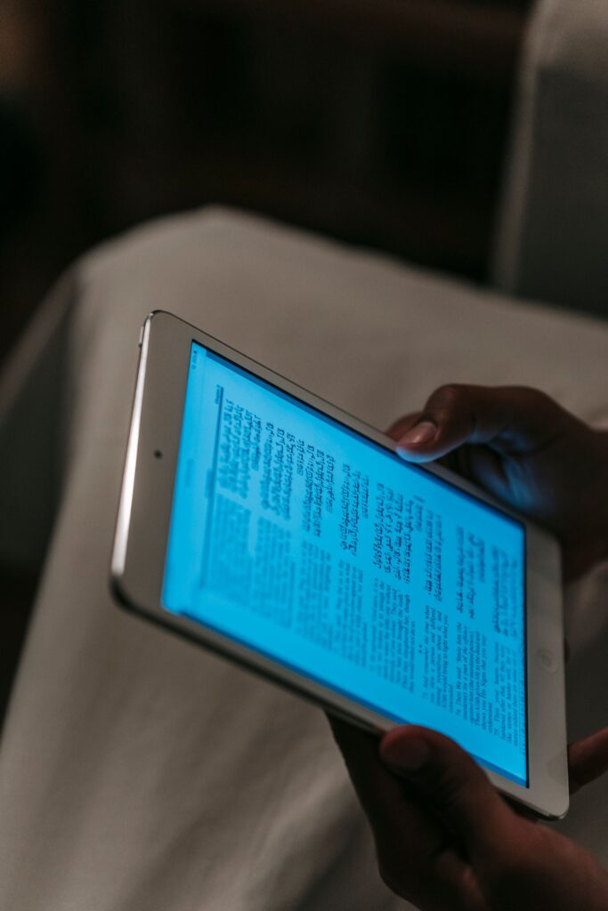 現在の画像: From above of crop unrecognizable person in white clothes browsing tablet in dark room