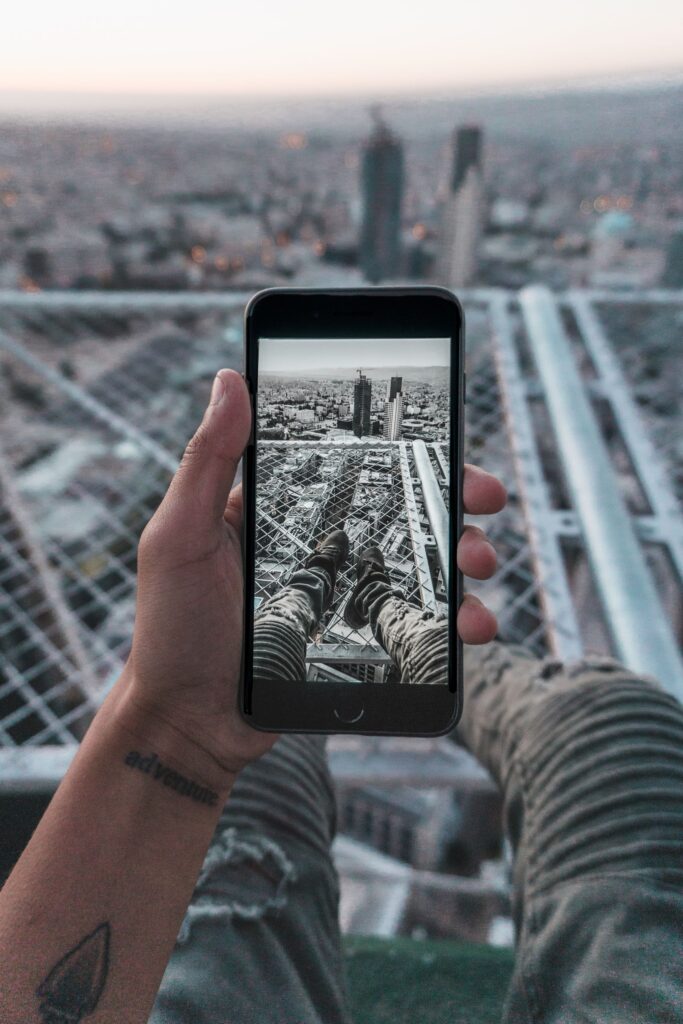 現在の画像: Hand holding smartphone capturing cityscape of Amman, Jordan from rooftop perspective.