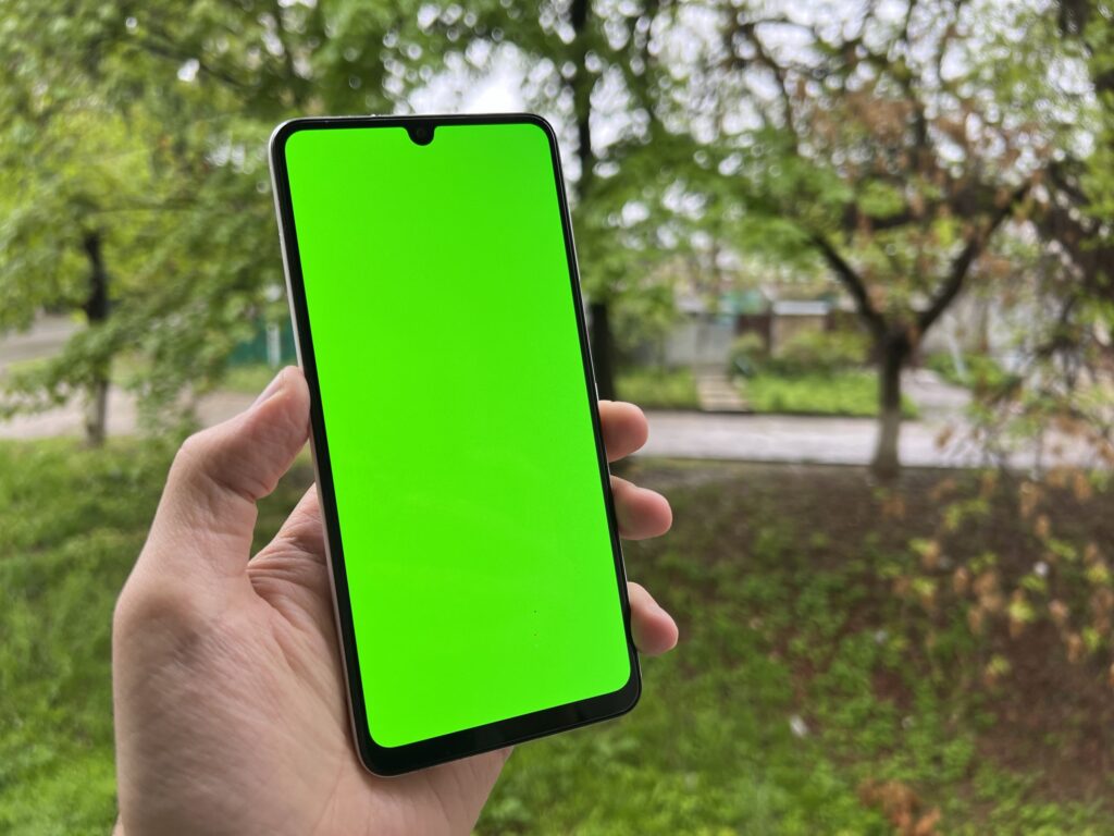 現在の画像: Hand holding smartphone with green screen outdoors, ideal for content overlay.