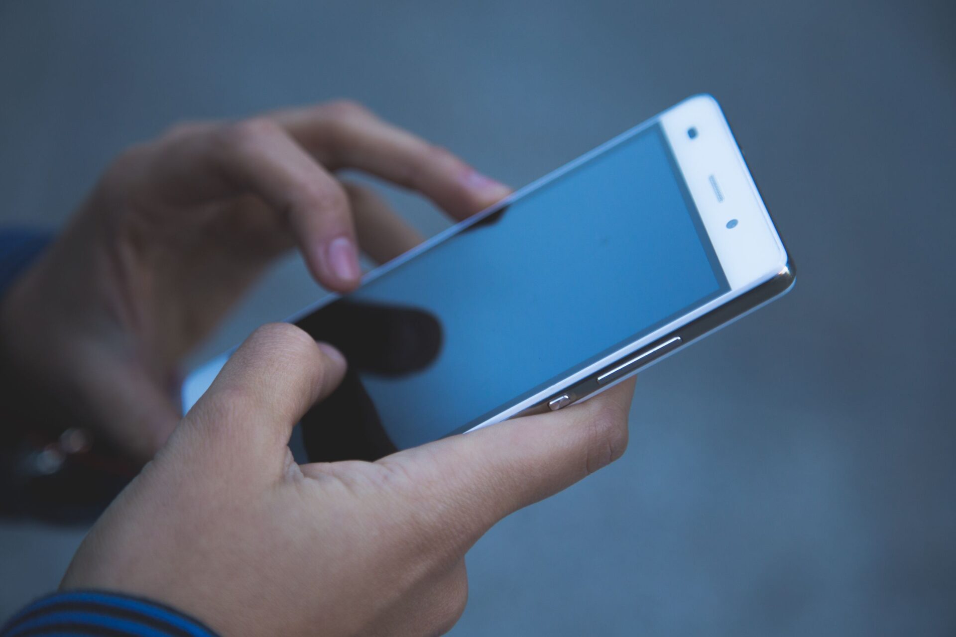 Hands holding a smartphone outdoors, showcasing modern communication technology in a casual setting.
