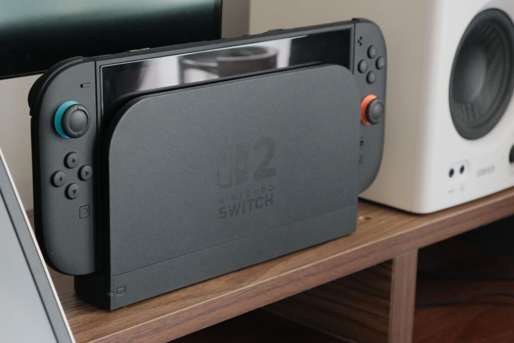 現在の画像: Nintendo console docked among speakers and a monitor on a wooden shelf.