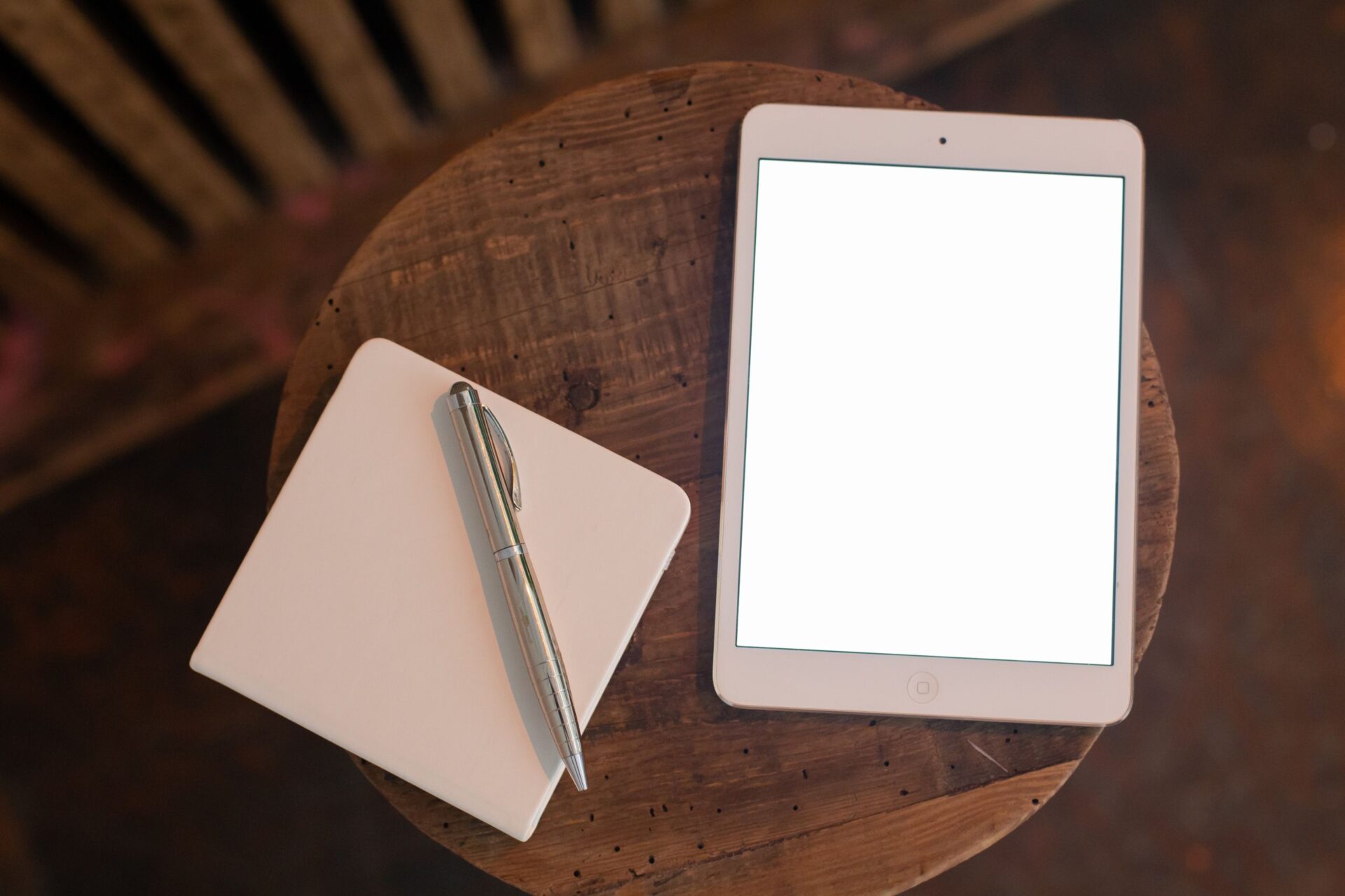 Overhead view of a tablet with blank screen and notebook with pen on wooden table.