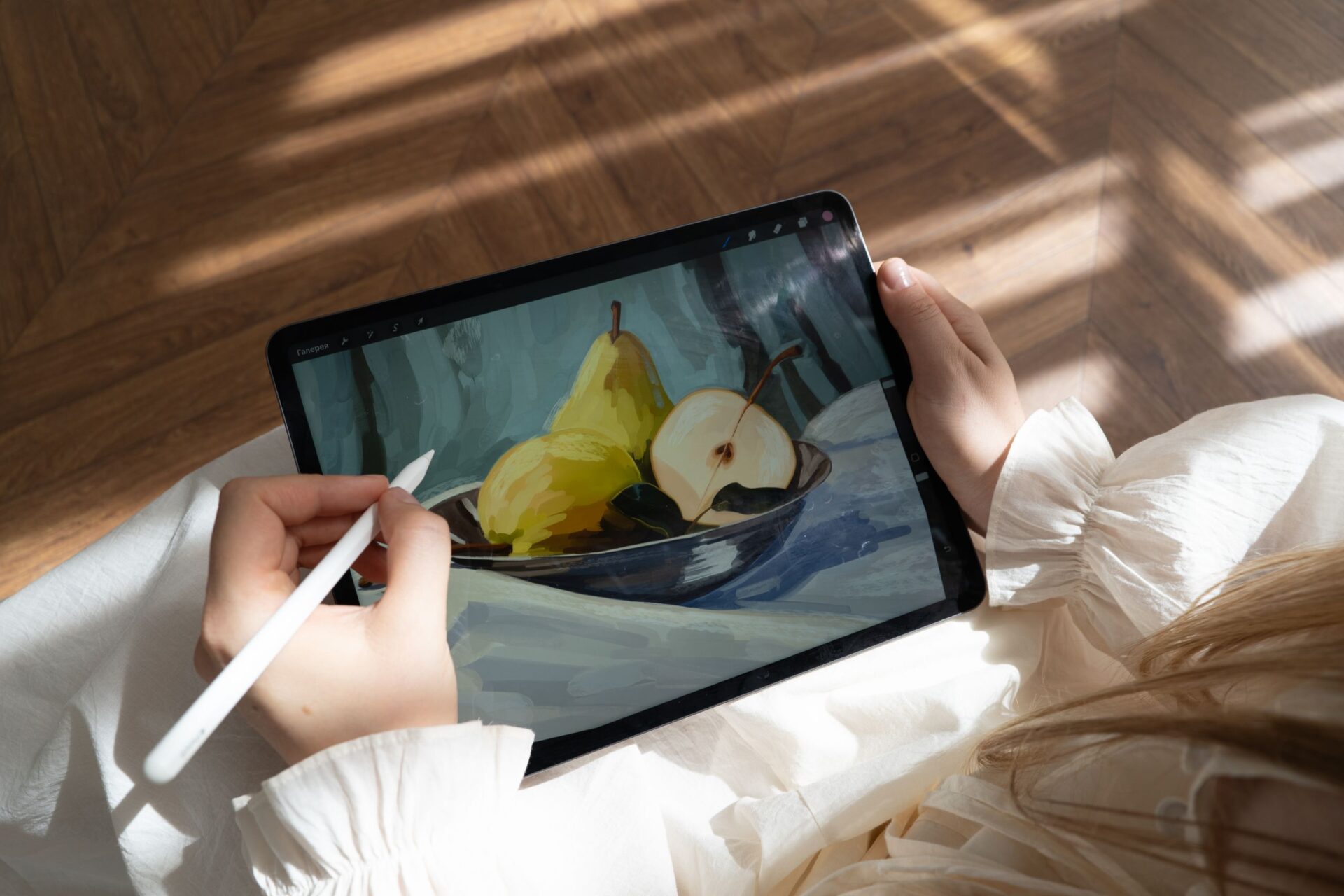 Person drawing pears on a tablet using a stylus in a sunlit room. Modern digital art creation.