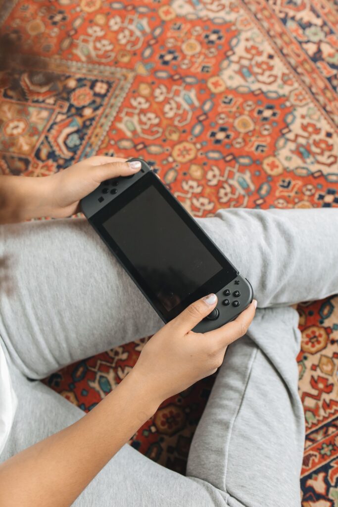 現在の画像: Person sitting on rug holding a Nintendo Switch, ready to play a game.