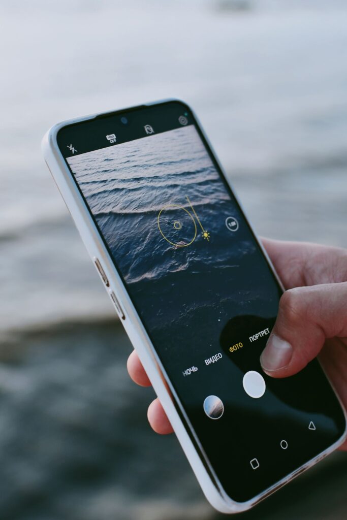 現在の画像: Person using smartphone to photograph waves on the beach.