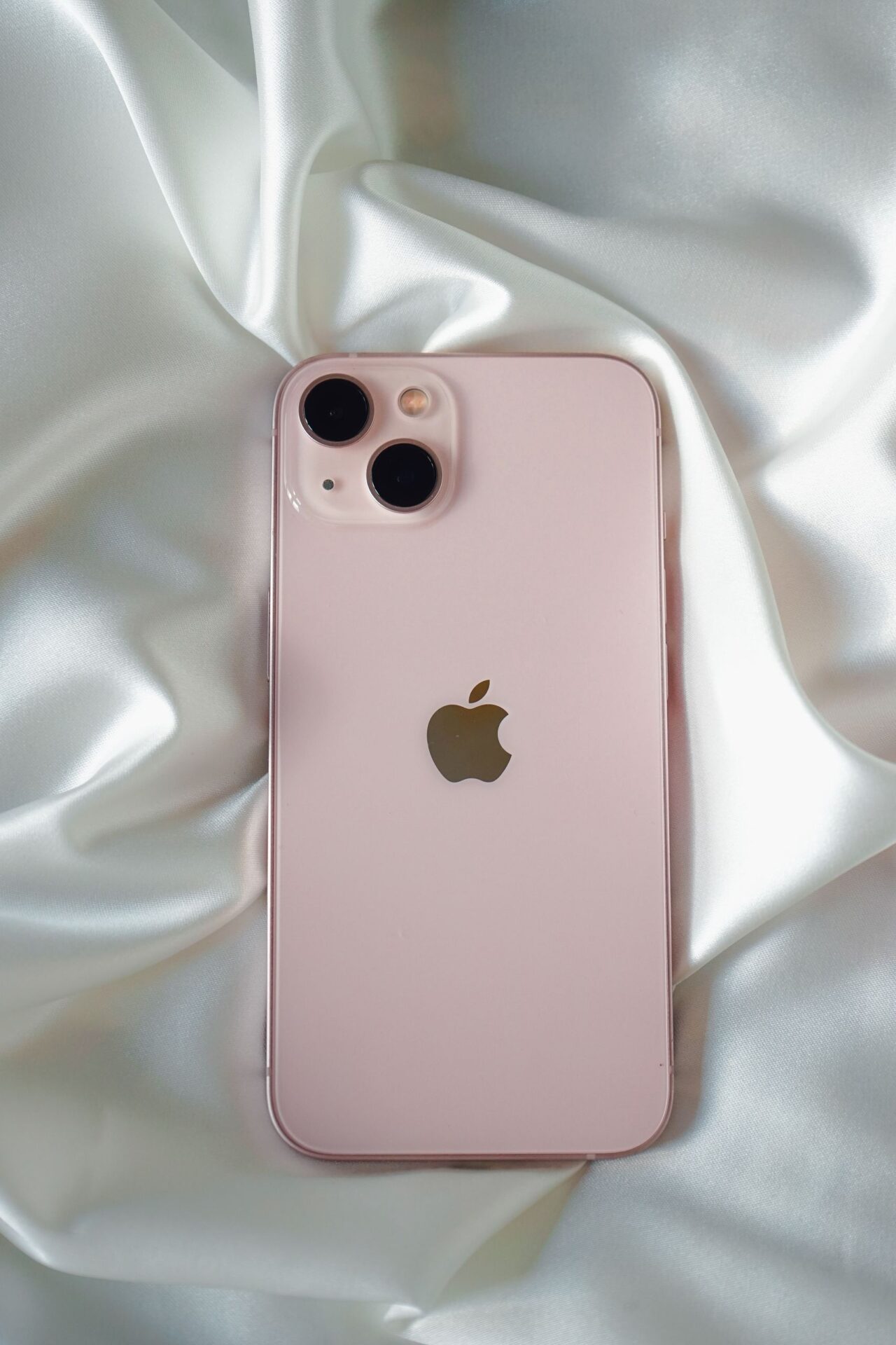 Pink smartphone with dual cameras placed on luxurious white satin fabric.