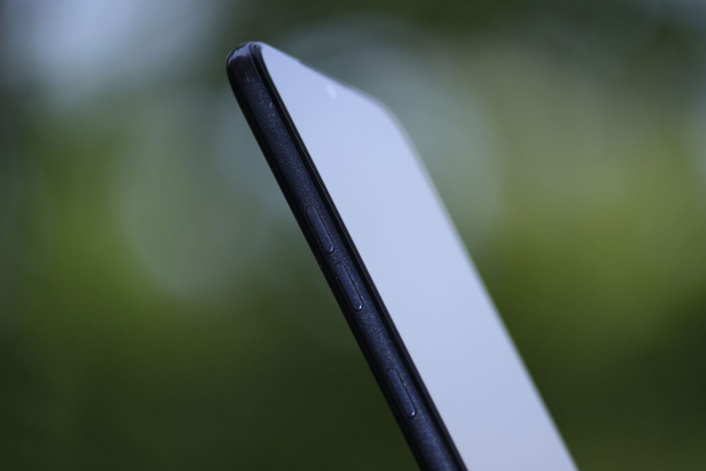 現在の画像: Side view of a sleek smartphone with a blurred green background, highlighting its slim design and buttons.