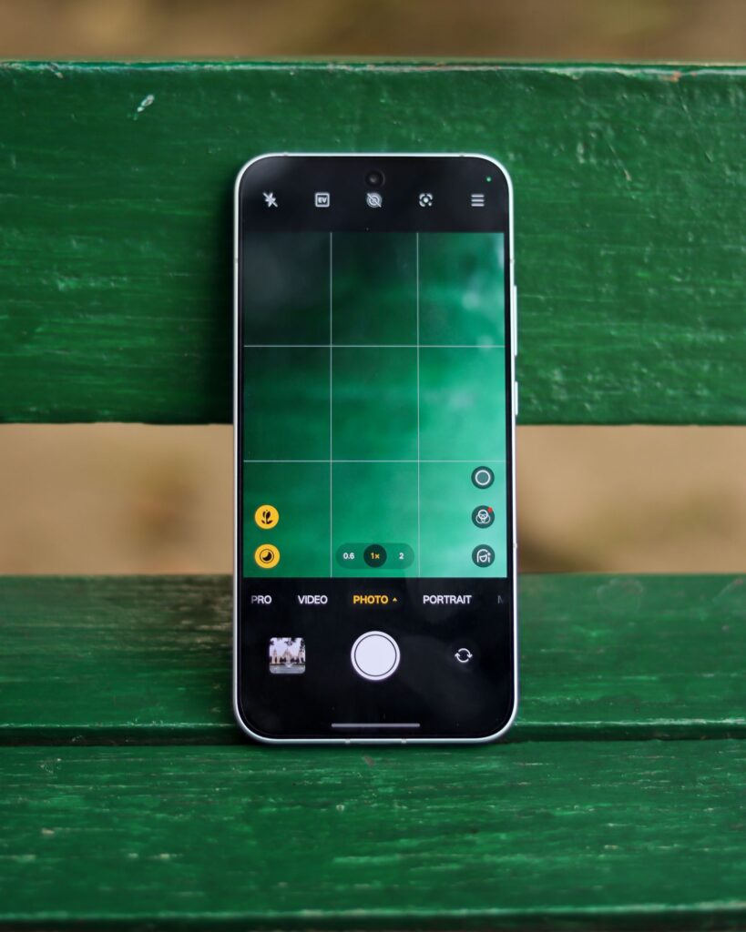 現在の画像: Smartphone displaying camera interface placed on a vibrant green wooden bench outdoors.