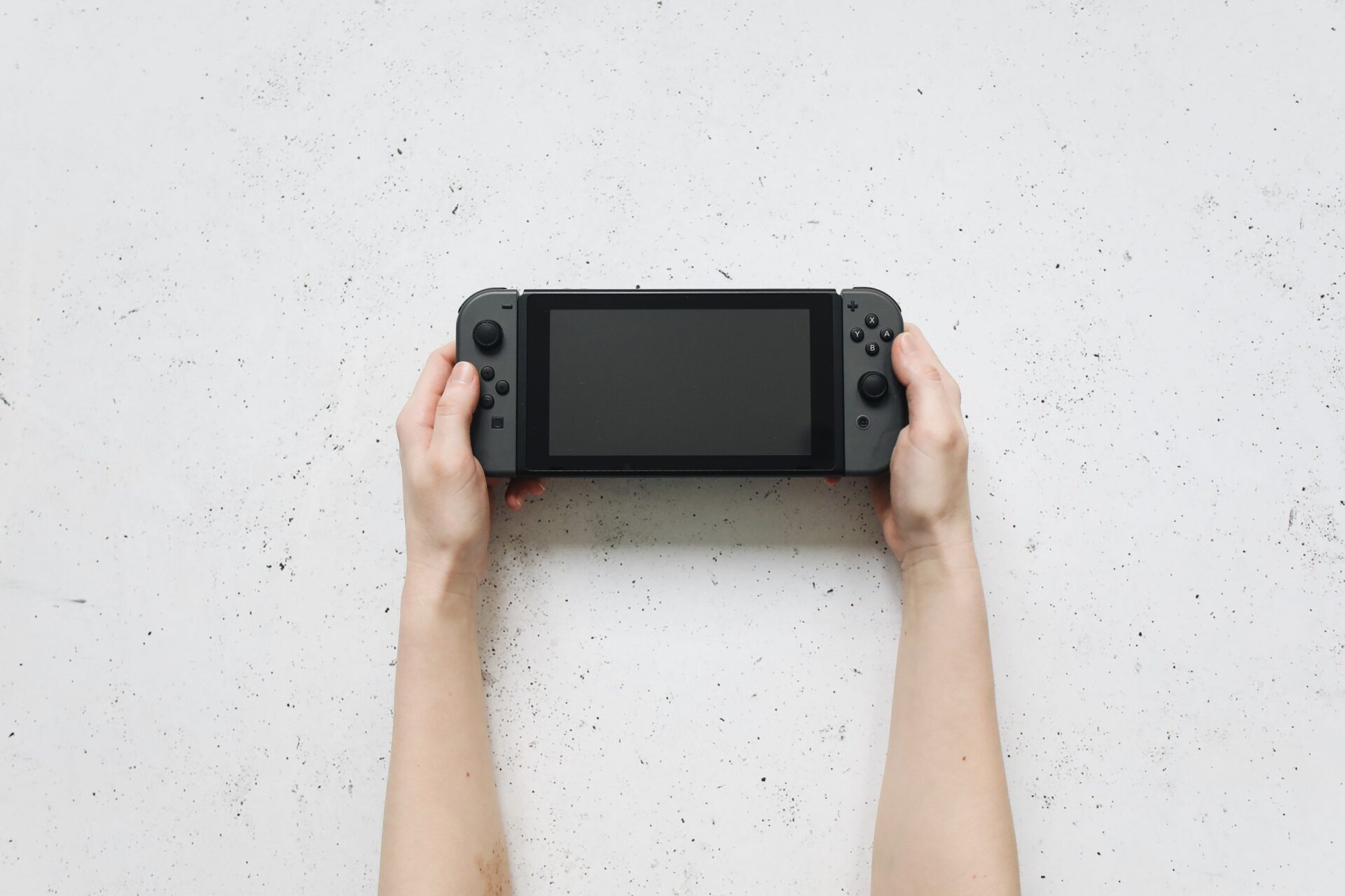 Top view of hands holding a portable gaming console against a textured white background.