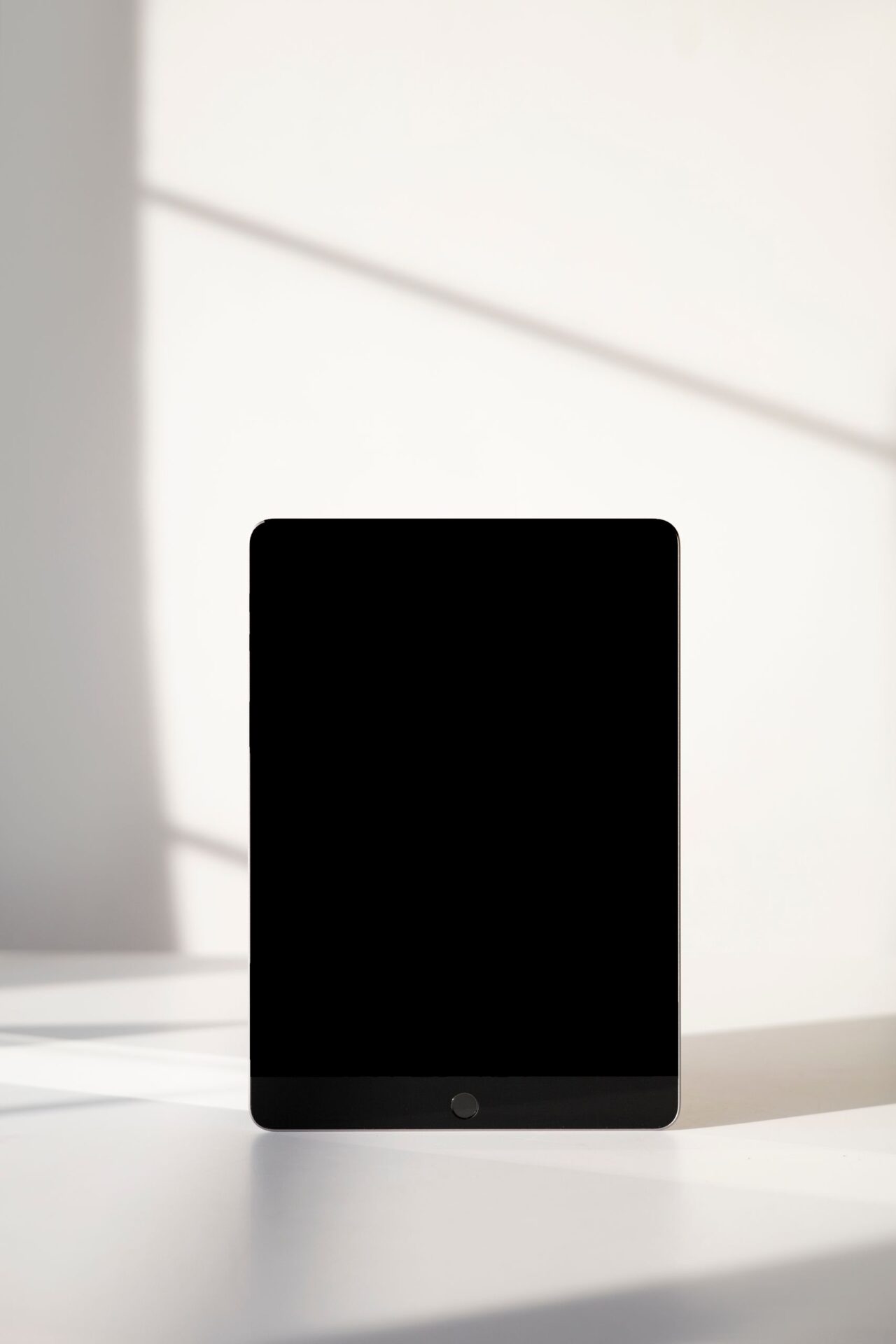 Vertical shot of a digital tablet mockup on a sunlit table with shadows.