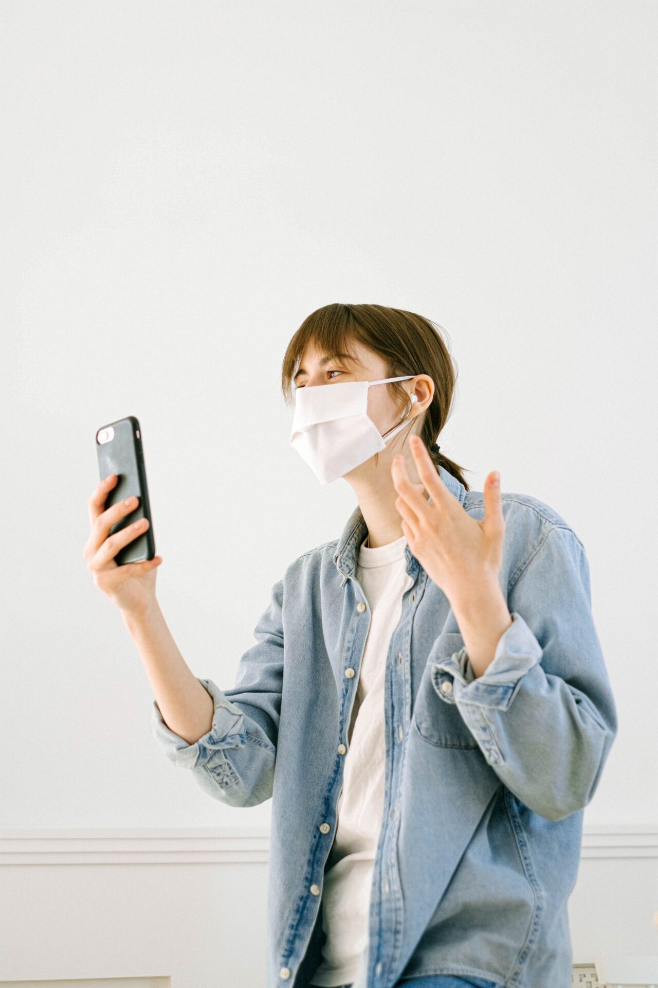 Woman wearing a face mask using her smartphone indoors for a video call.